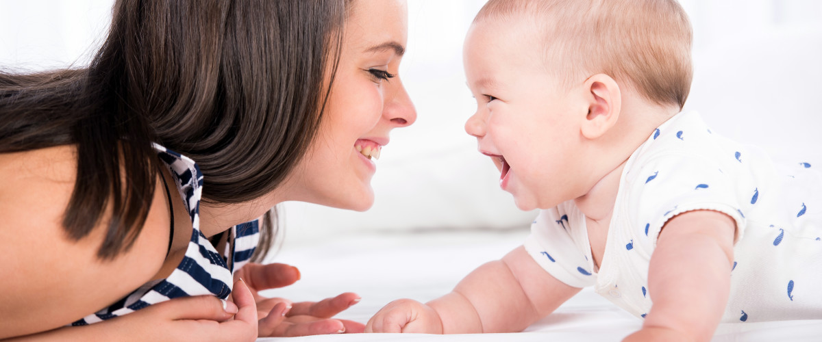 Mother and Baby lying on stomachs looking at each other laughing.